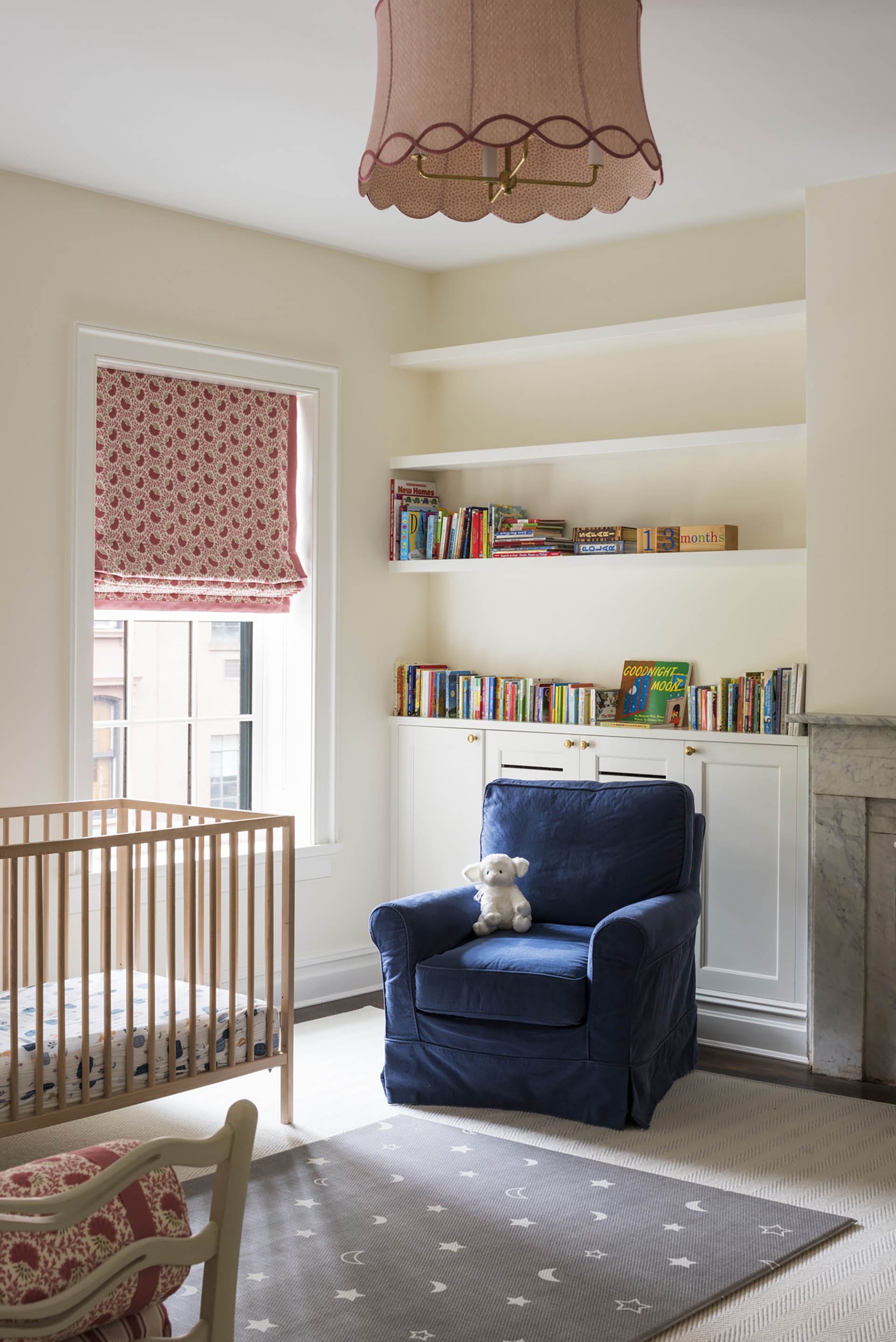 Nursery with a crib, pink shades, and a blue velvet armchair.