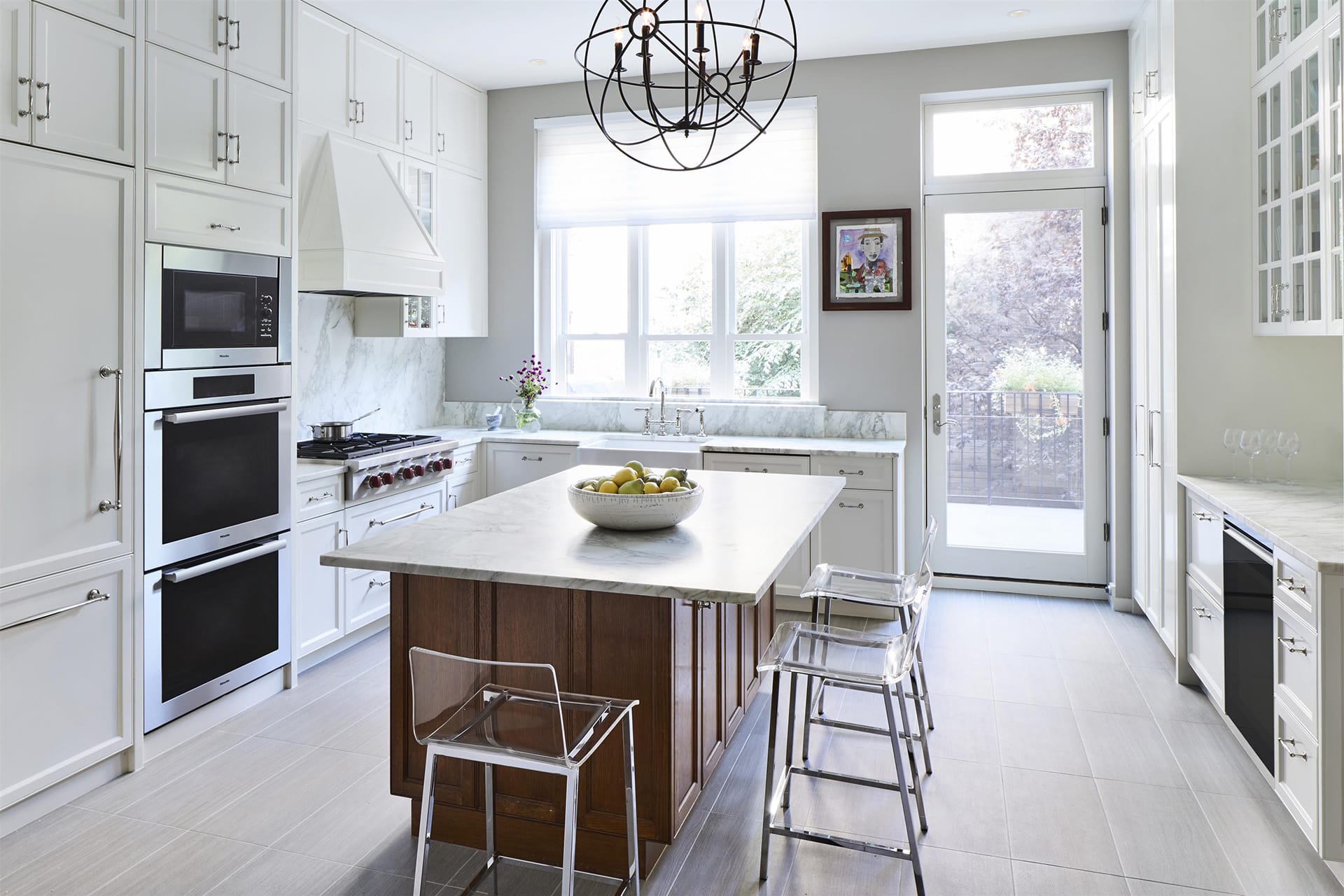 Parlor-level kitchen with white cabinetry, a double oven, wood an white marble island, and clear bar stools