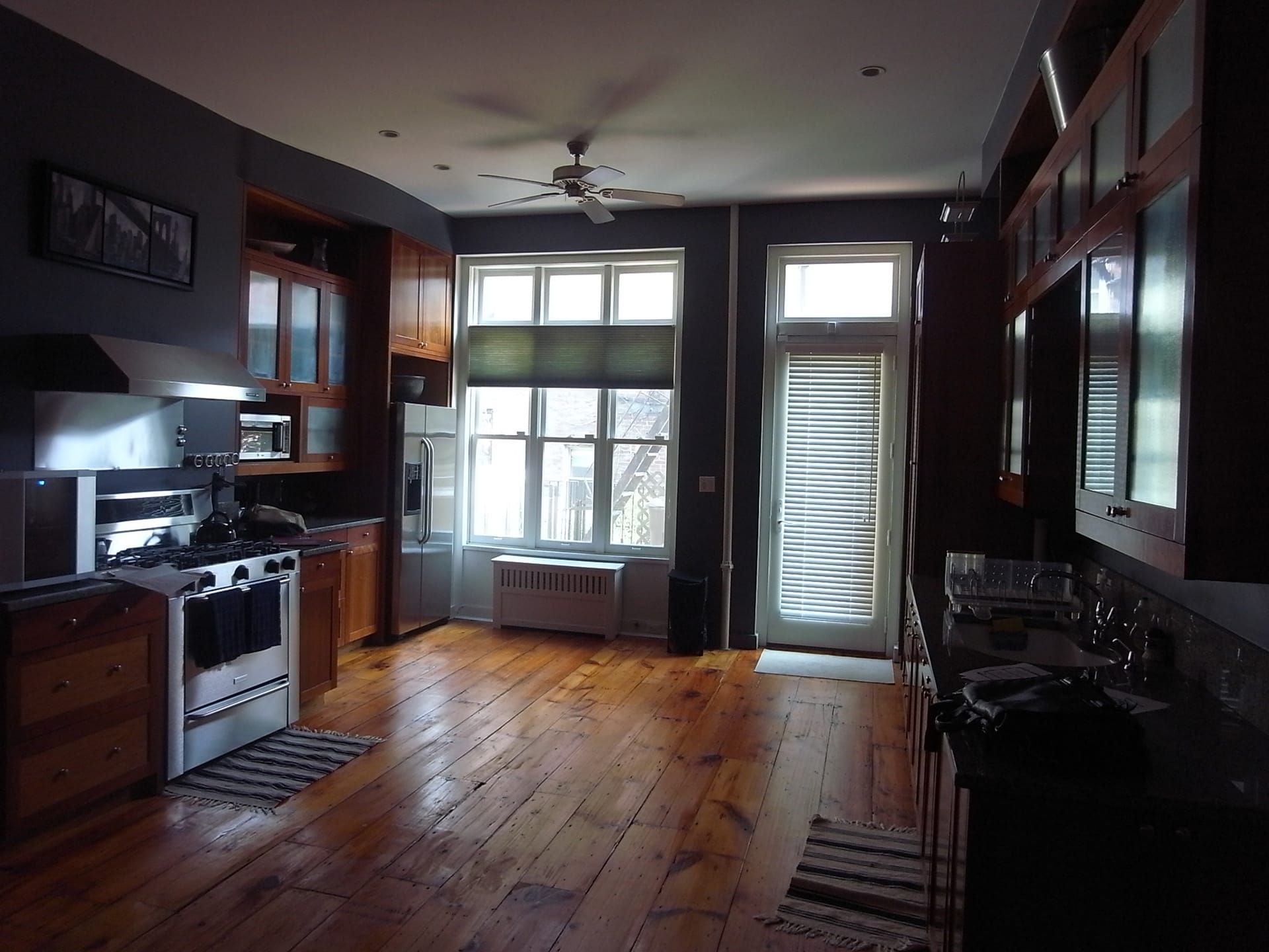 Parlor level kitchen with dark wide plank floors and dark wood cabinetry and a ceiling fan.