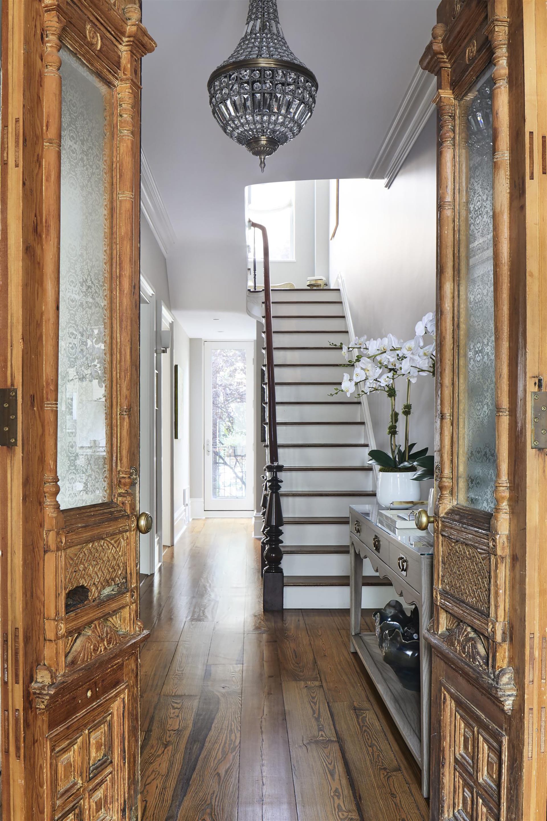 Restored historical wood doors open to reveal the entryway of a Cobble Hill townhouse with wide plank wood floors and a chandelier