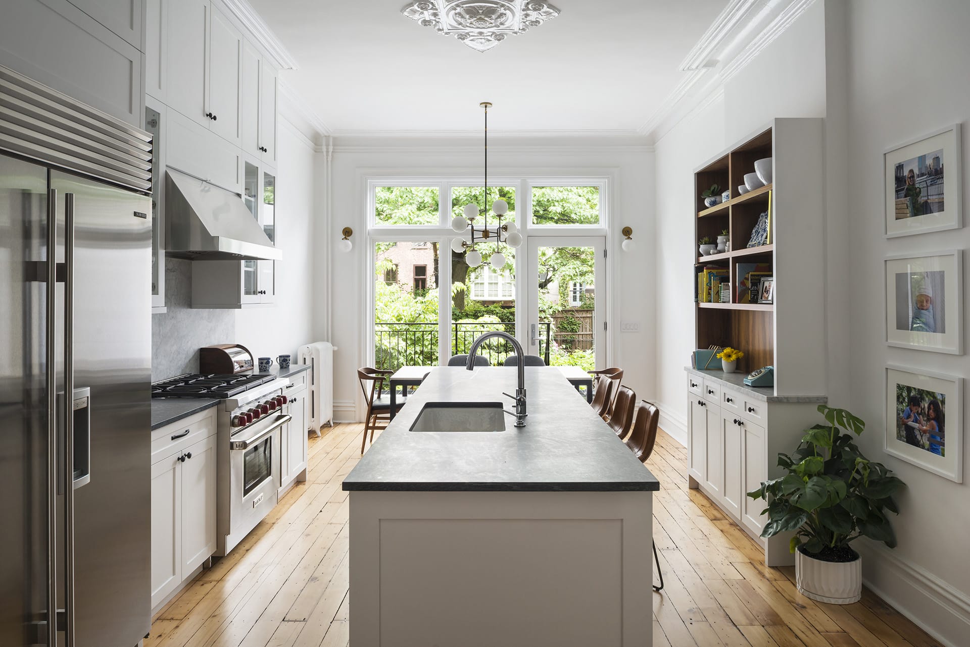 Renovated parlor floor of a Cobble Hill townhouse with natural wood floors, large glass doors leading to the backyard, and all-white walls and cabinetry.