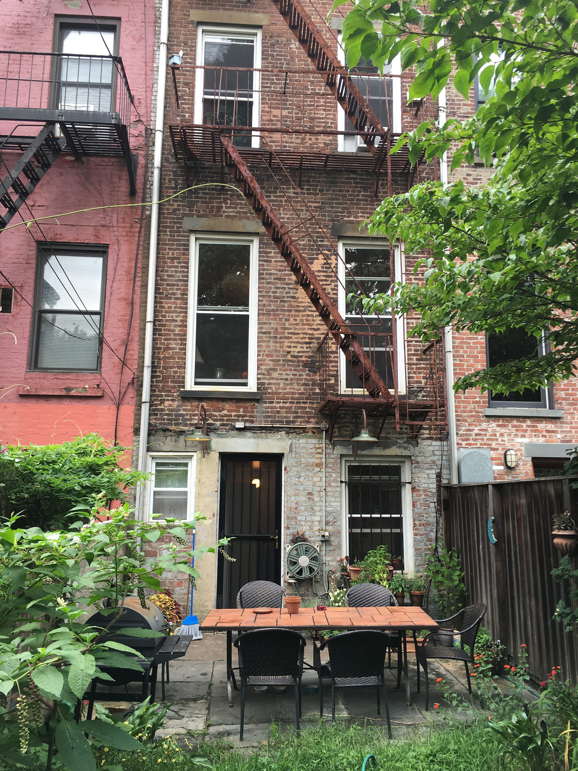 Rear facade of a Cobble Hill townhouse with fire escape, outdoor table and chairs, and back yard.