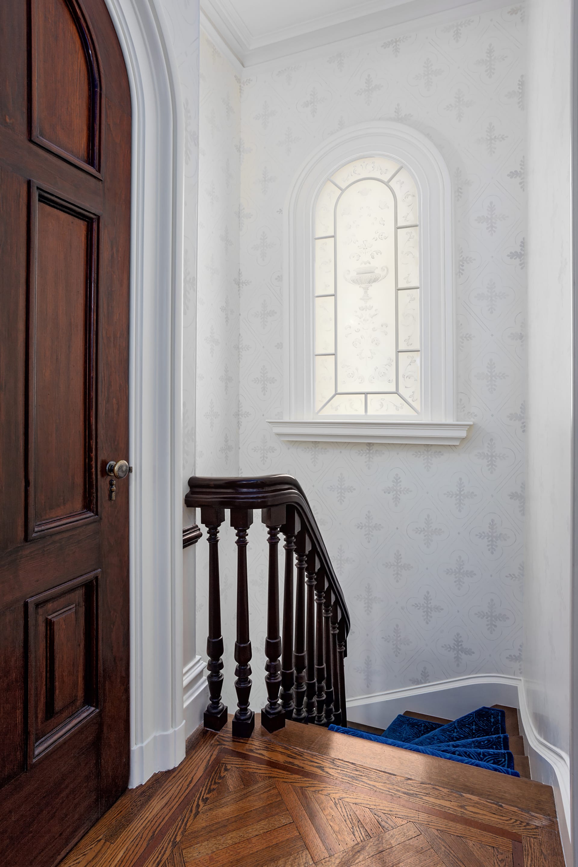 Stair hallway after renovation with artificially-lit etched window, white wallpaper, and royal blue stair runner