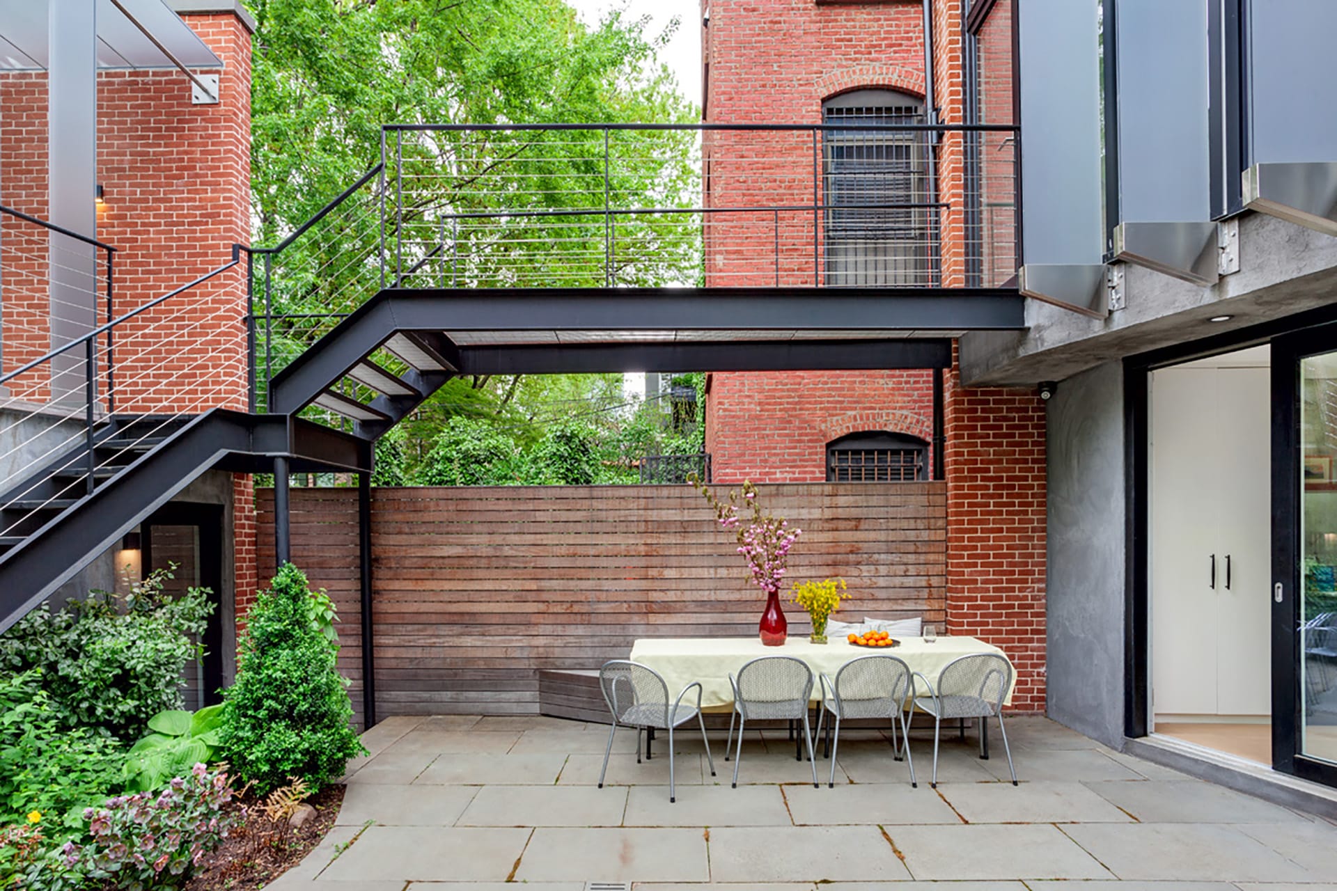 Rear yard of a Park Slope townhouse in between the main home and detached garage, with a suspended catwalk, picnic table, and landscaping