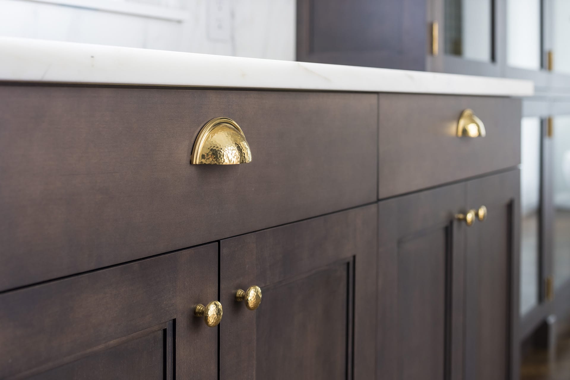 Detail of custom wood cabinets with hammered bronze fixtures and white marble countertops