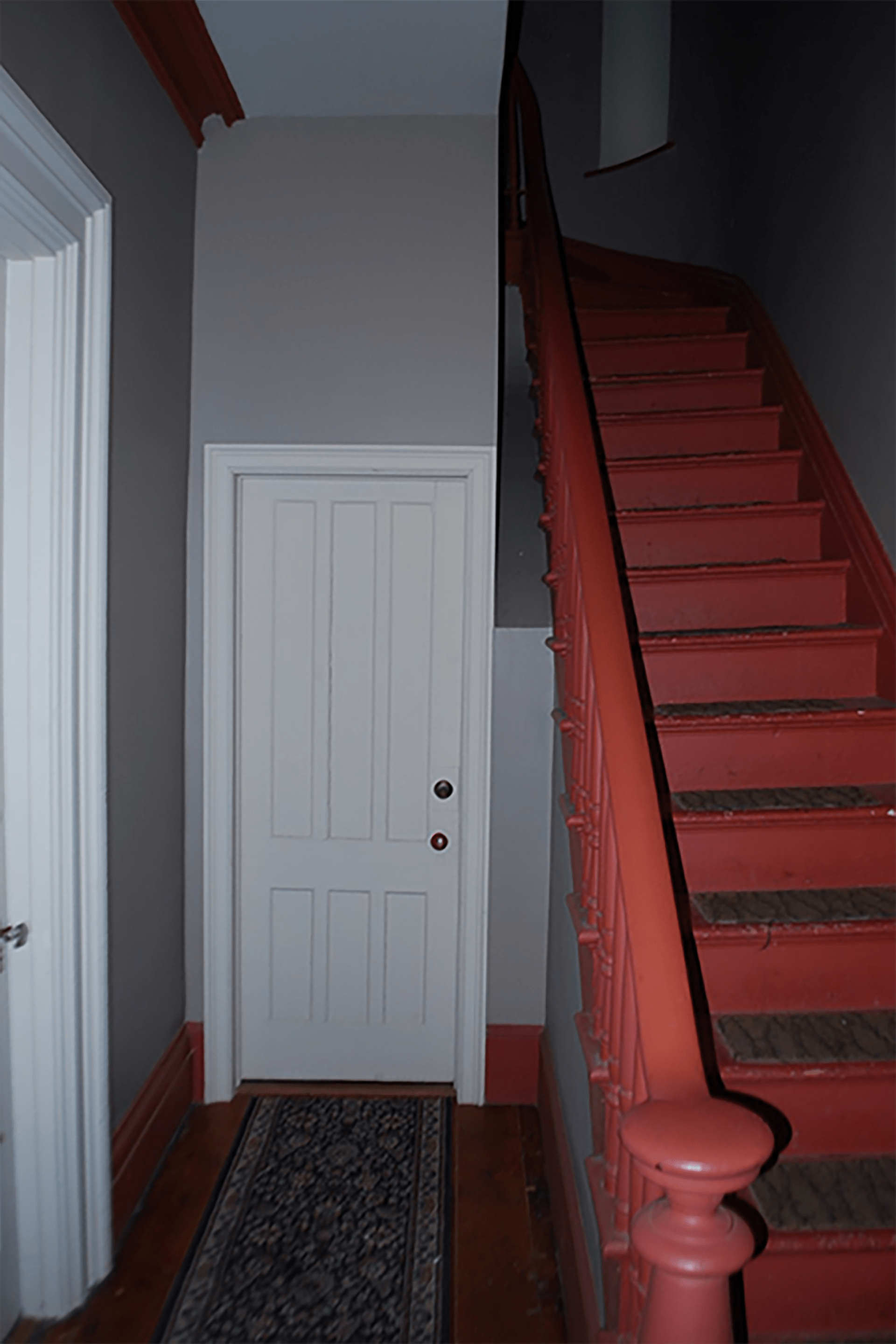 Red painted staircase and its landing with grey walls and white doors.