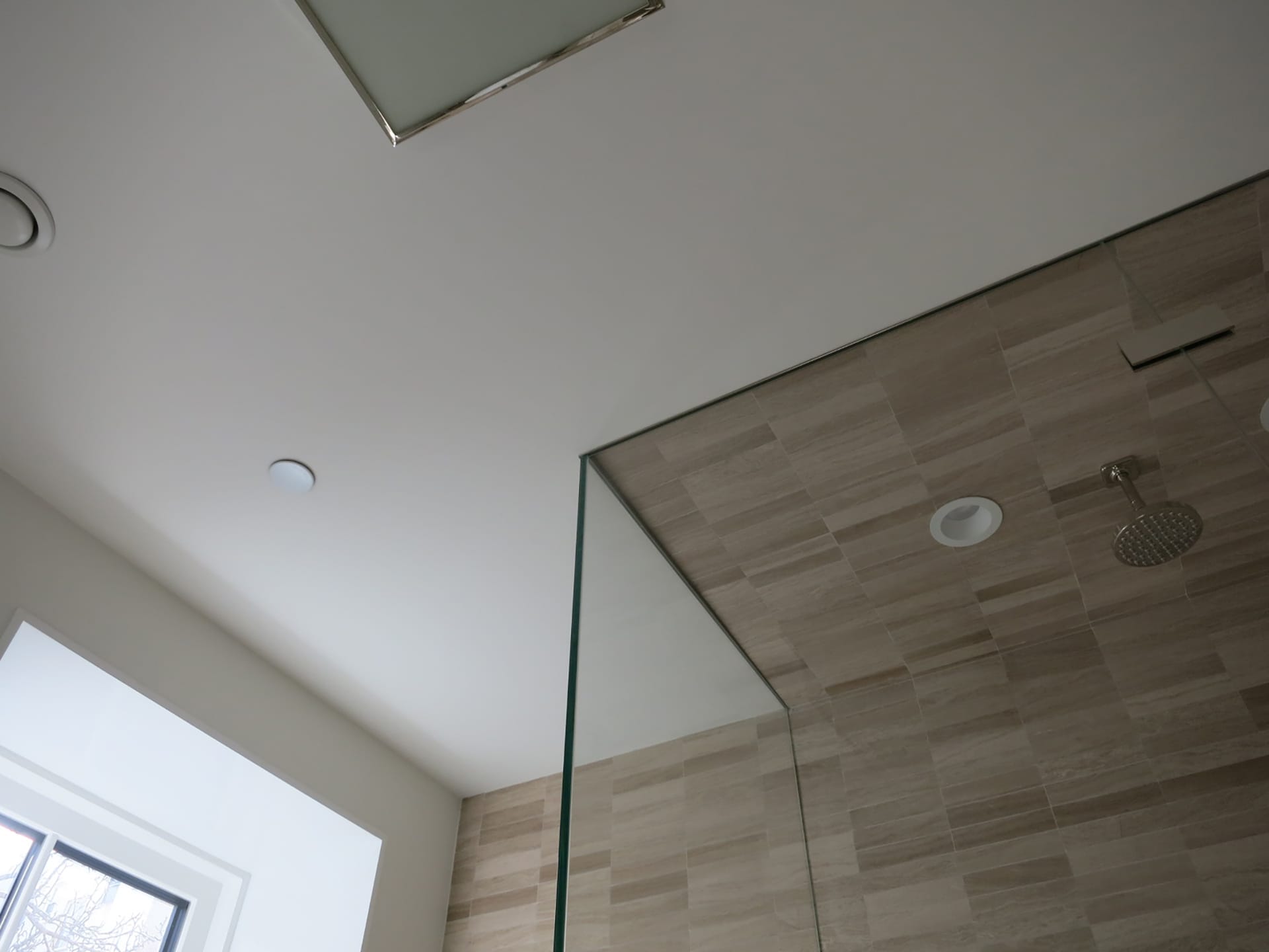Corner of a glass steam shower with recessed ceiling tiles.