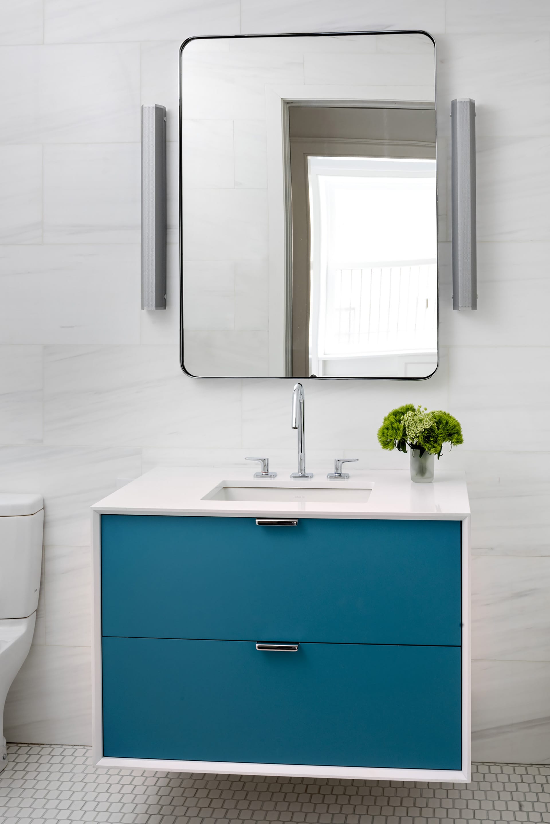 Floating vanity in an all-white bathroom with blue drawers