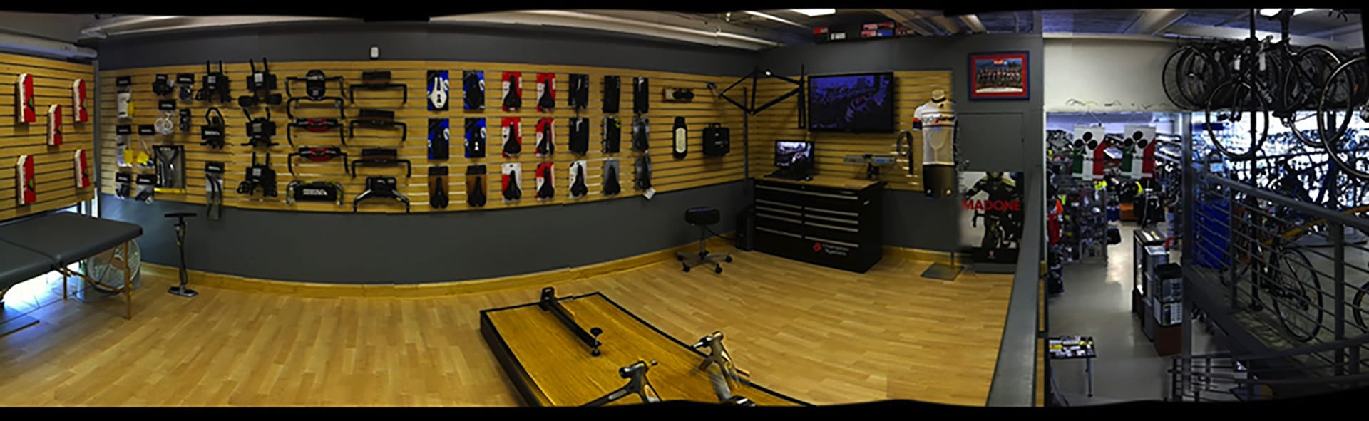 Panorama photo of a bike fitting shop with wood paneled walls and wood floors, elevated from the sales floor on the right.