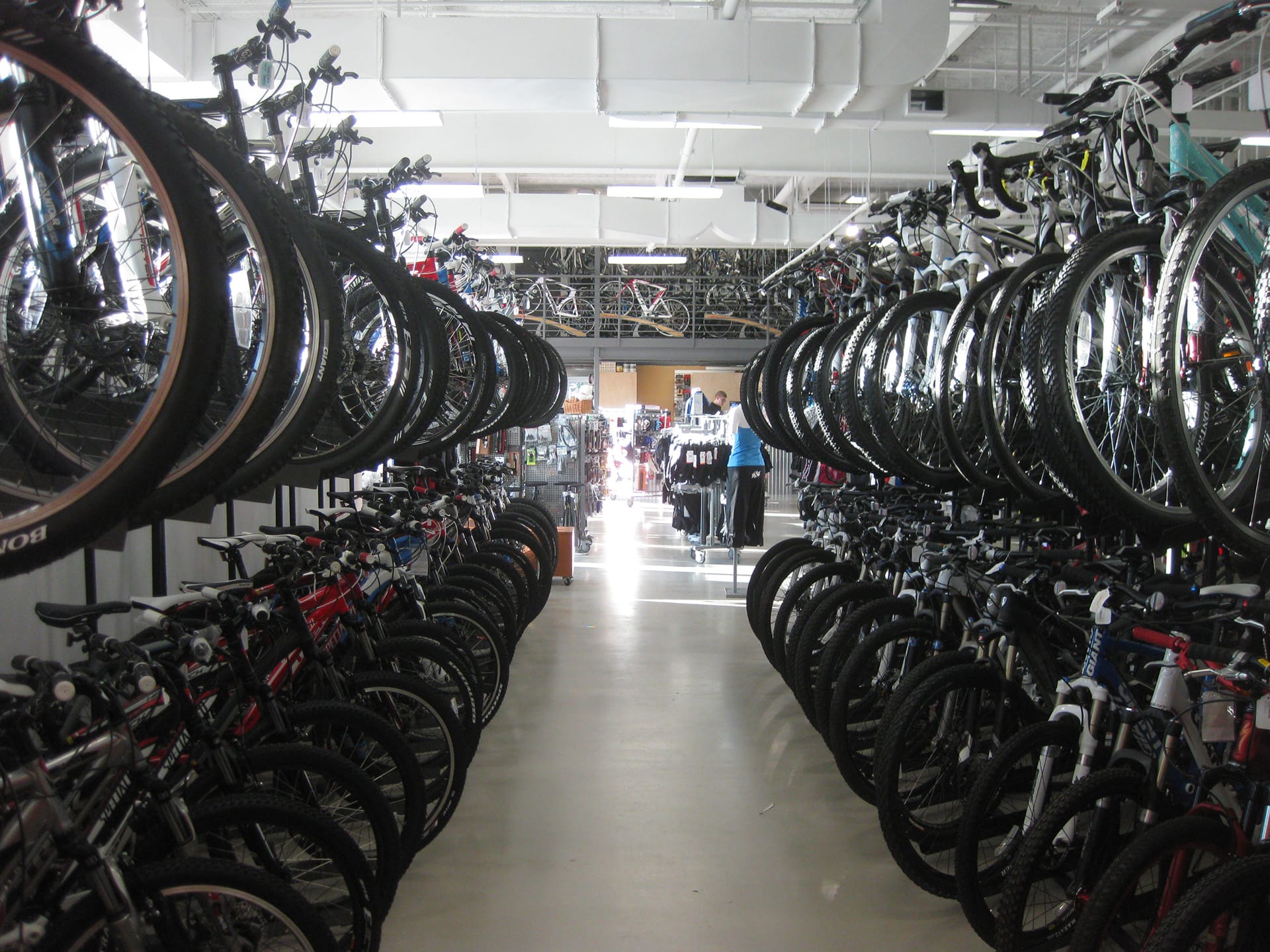 Aisle of a bike shop. Two rows of bikes, one on top of the other, line both sides of the aisle.