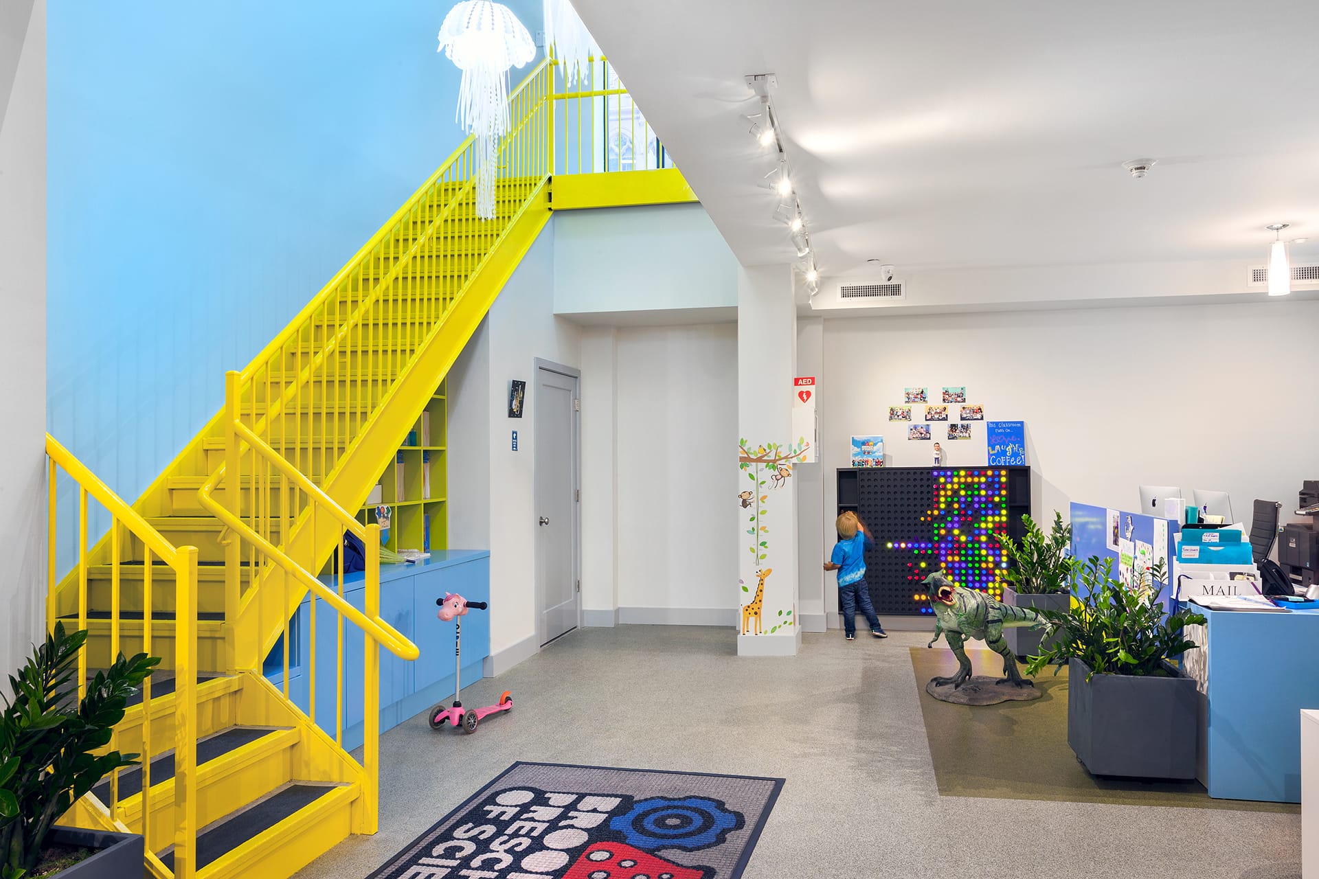 Bright yellow staircase leading to an office space with one bright blue accent wall and a jellyfish light.