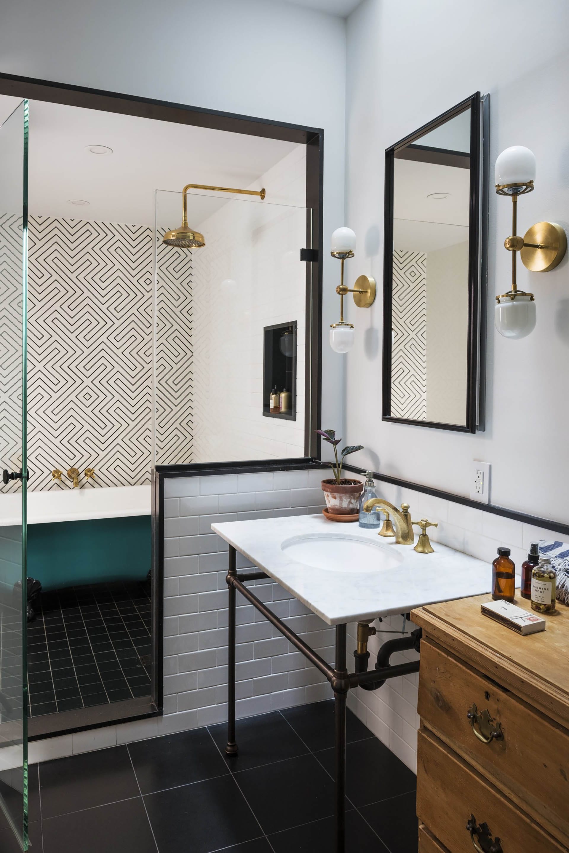 Bathroom with bronze fixtures, a teal freestanding tub and shower stall, and geometric wallpaper.