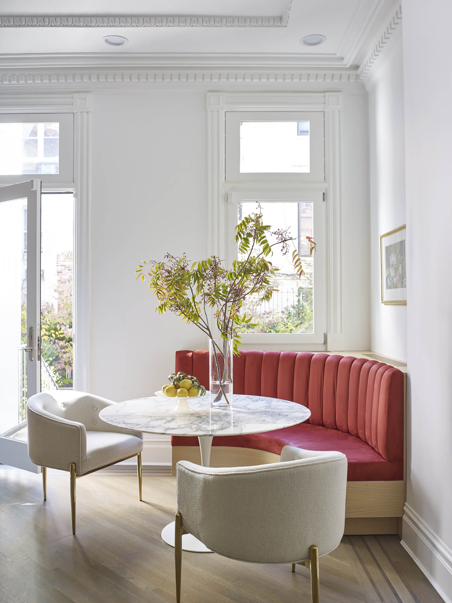 Red banquette in the breakfast nook of a restored kitchen with white painted walls and plaster molding