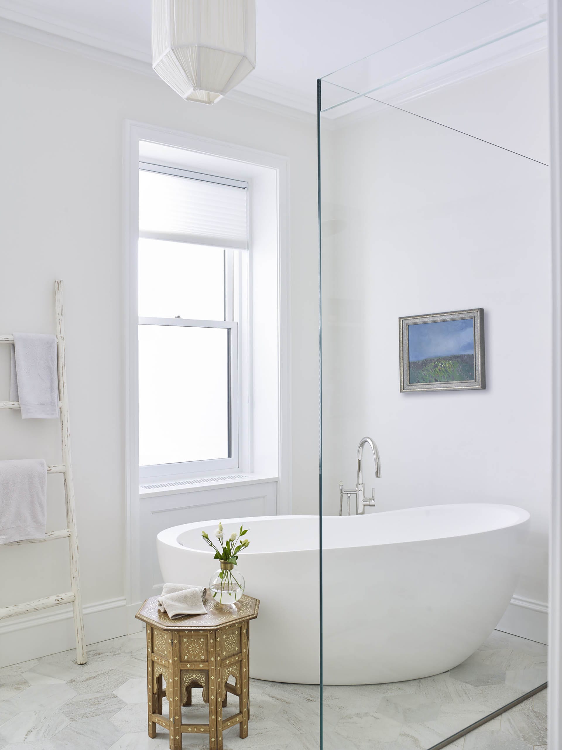 All white primary bathroom with a freestanding tub, shower stall, and painting of a meadow on the wall.