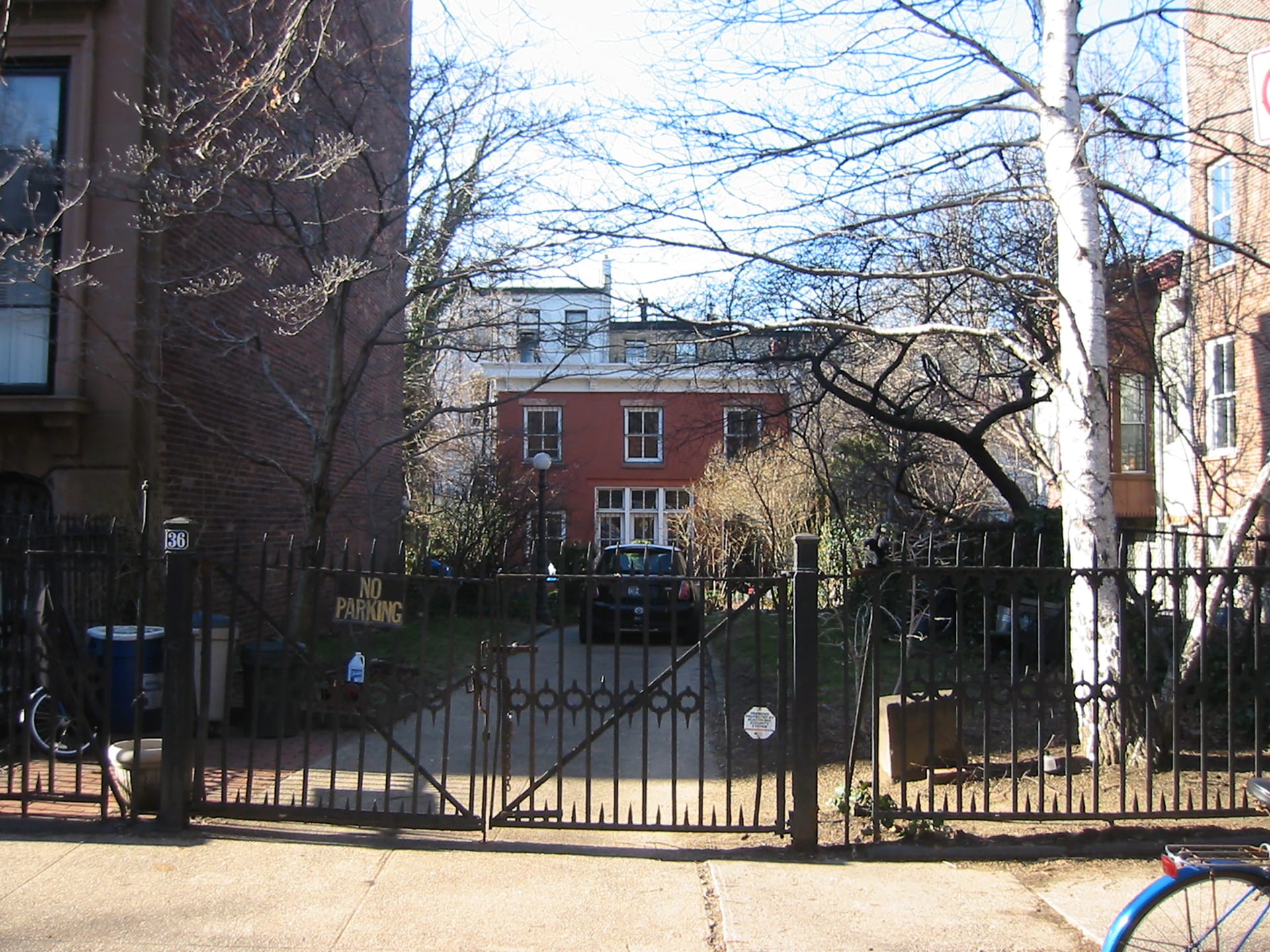 Street view of a rear-situated Cobble Hill carriage house with a front driveway, gate, and white trim.