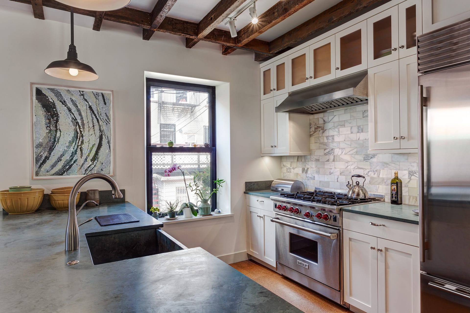 Renovated kitchen in a carriage house with blue countertops, stainless steel appliances, white cabinetry, and exposed ceiling beams.