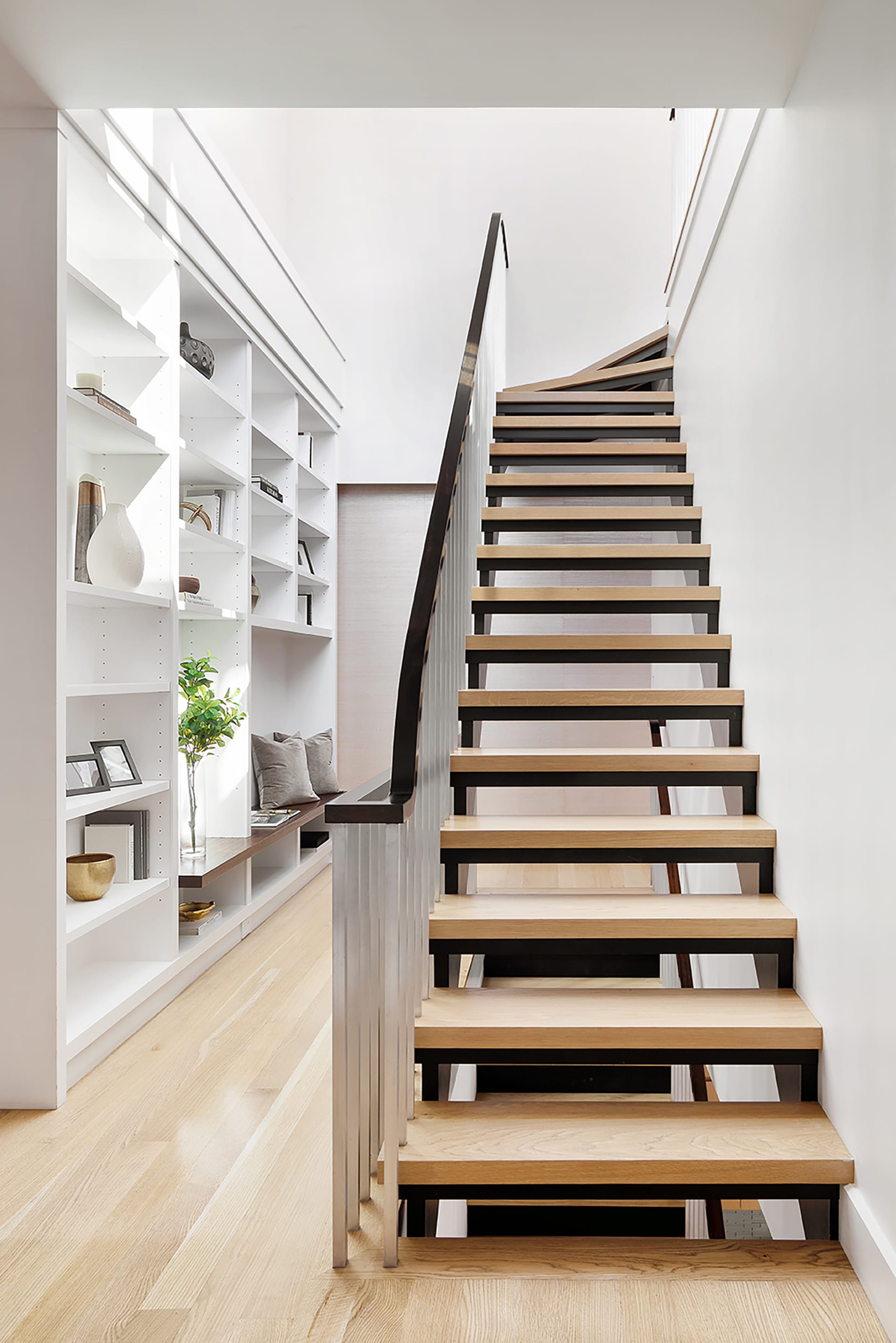 Open stringer, open riser staircase with light wood treads in a stair hallway with a wall of shelves