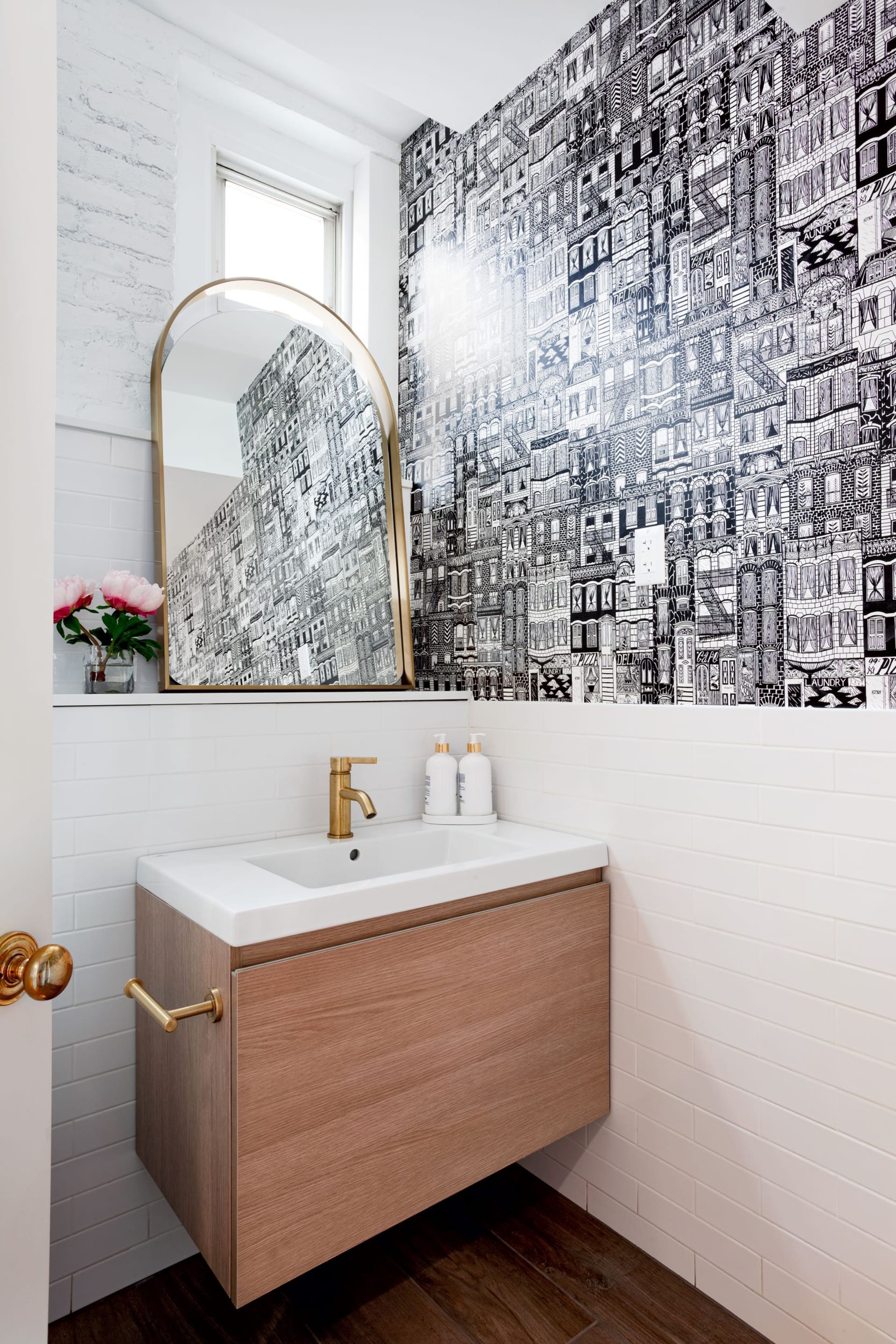 Powder room with a floating vanity, black and white townhouse-print wallpaper, and white subway tiles that reach chair-rail height.