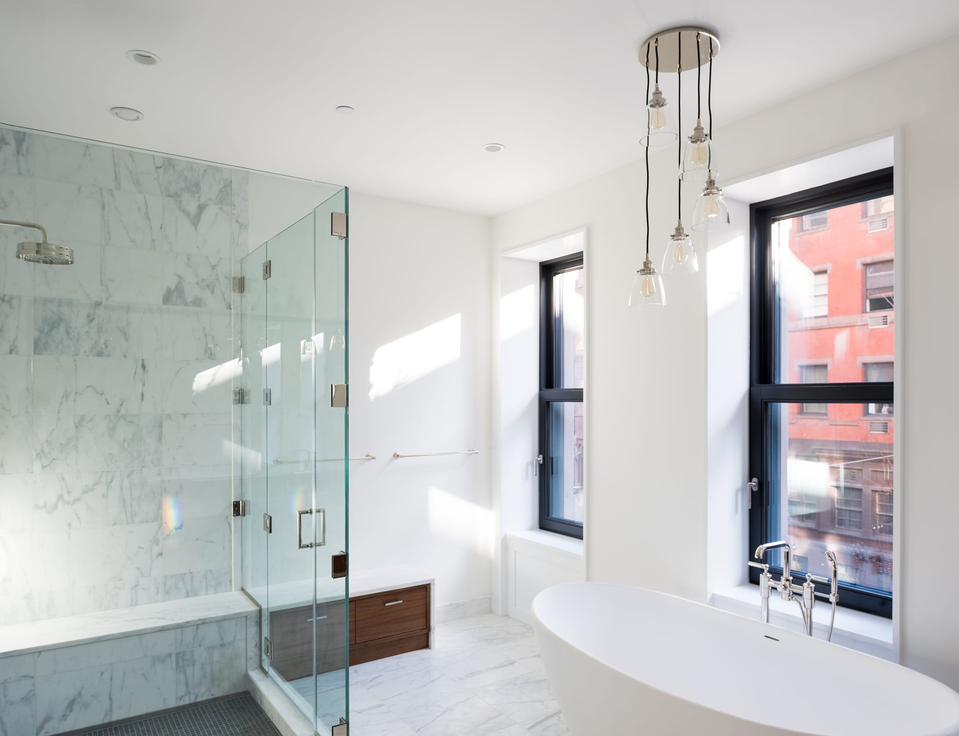 Shower stall, light fixture, and freestanding bathtub in the primary bathroom of an Upper West Side Passive House.