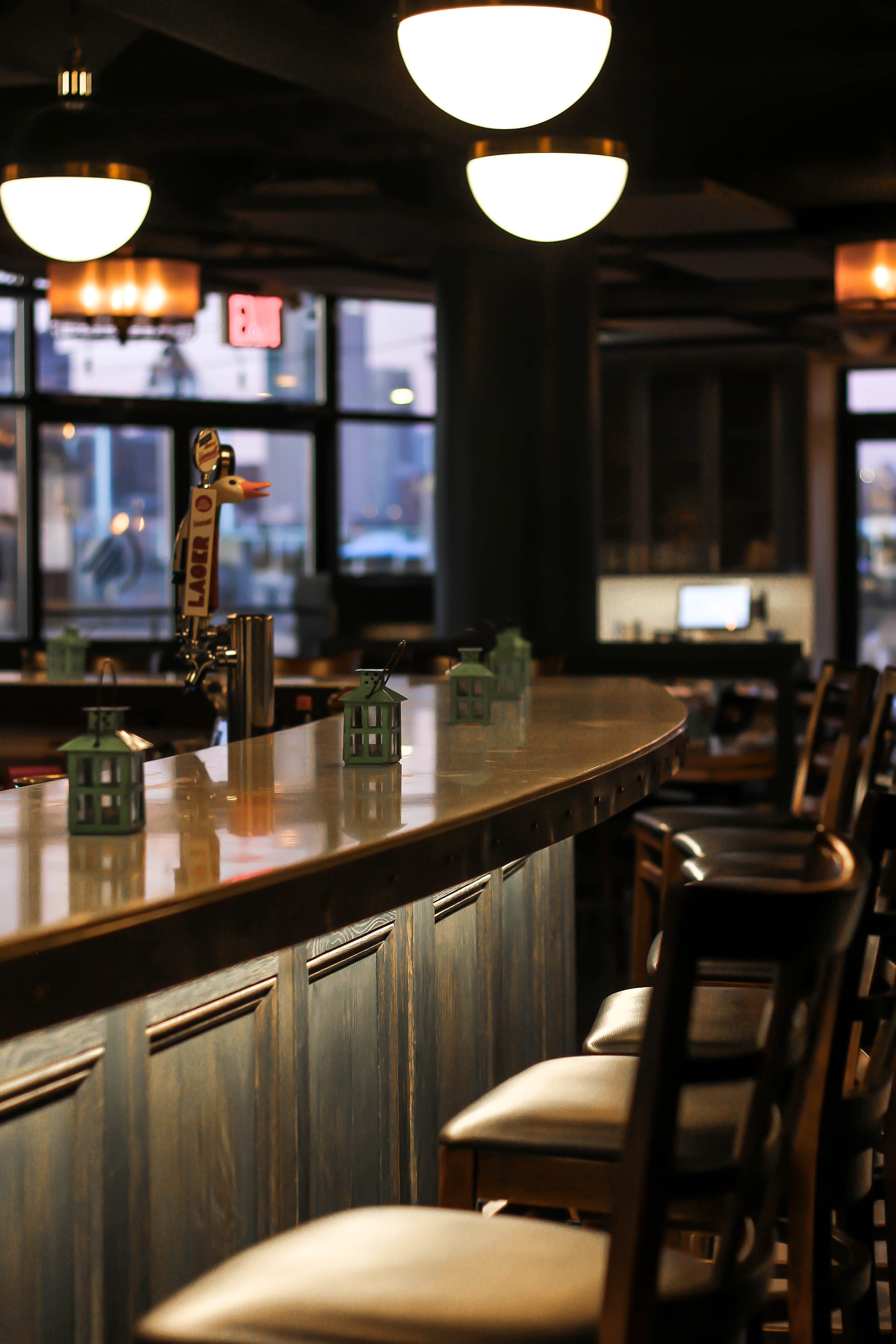 A row of barstools in front of a bar with green lanterns on top and alcove lighting underneath the bar.