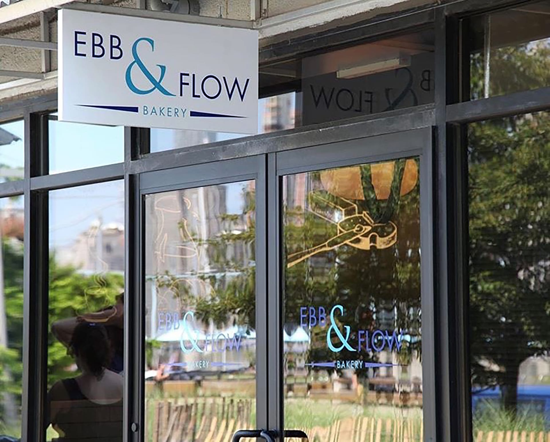 Glass storefront of the Ebb & Flow Bakery with a sign hanging above the door and a chalkboard sign next to the front doors.