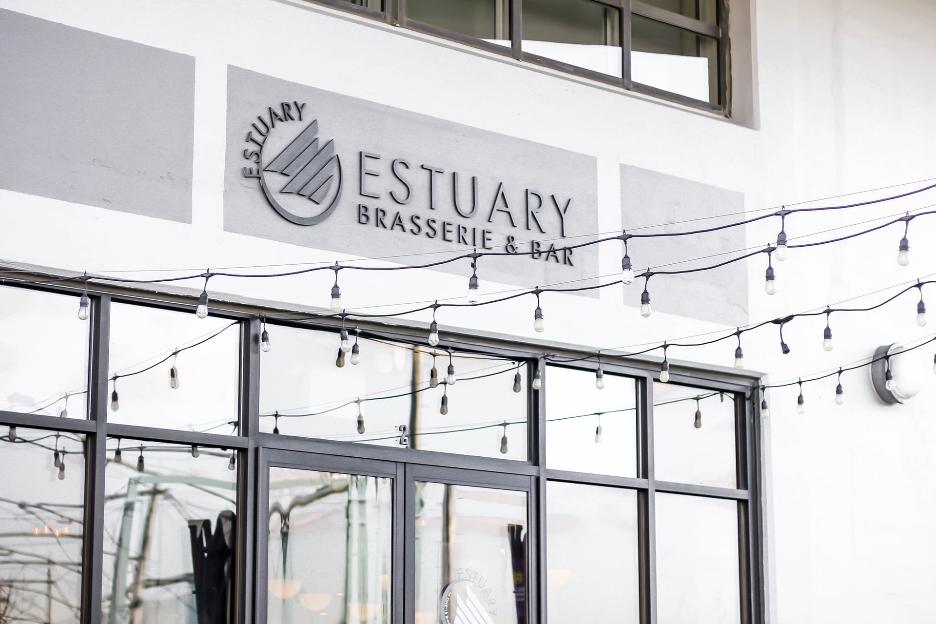 Exterior of the Estuary Brasserie & Bar with a row of string lights hanging in front of the door.