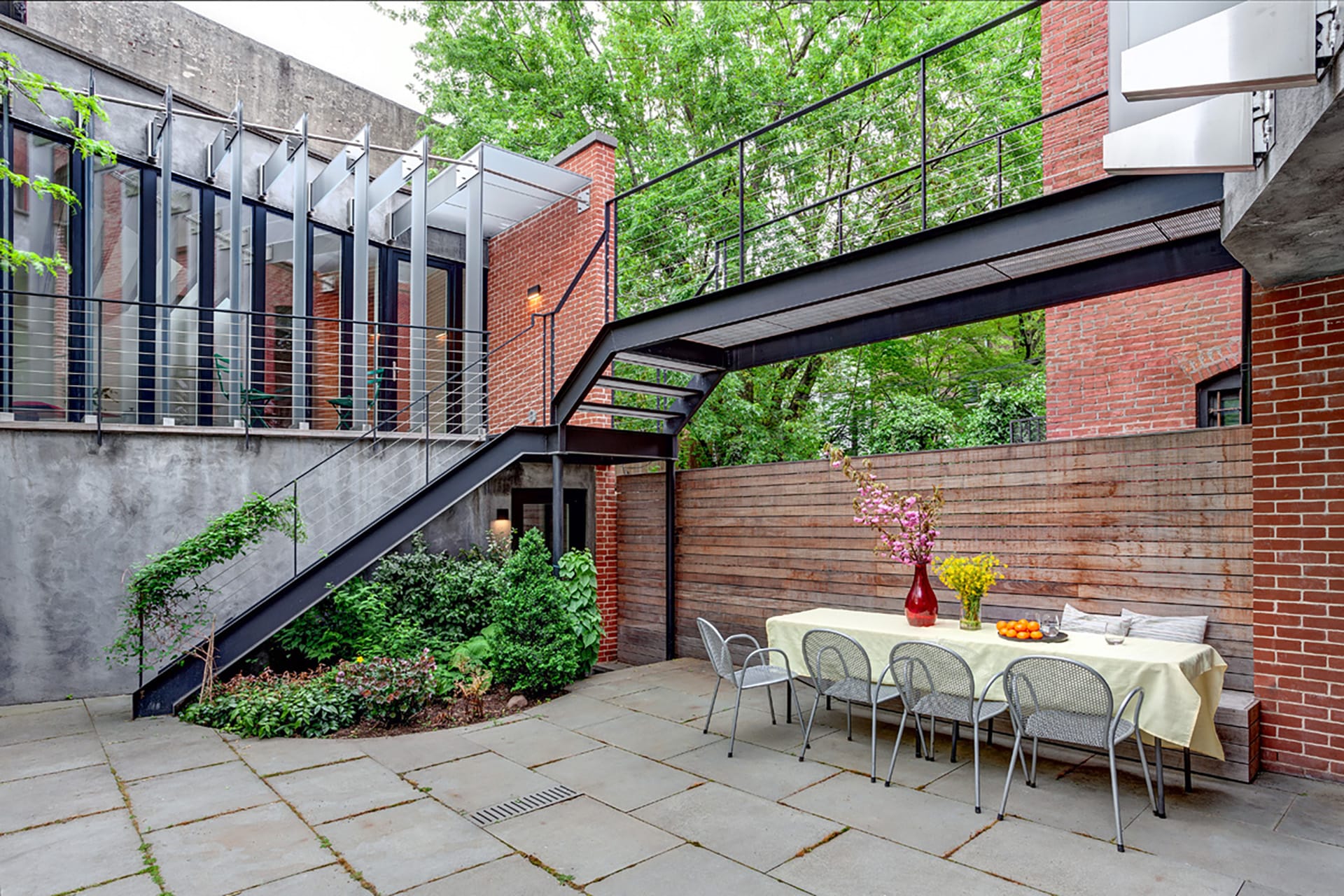 Courtyard between a townhouse and its separated garage with a suspended catwalk, bluestone pavers, and a picnic table