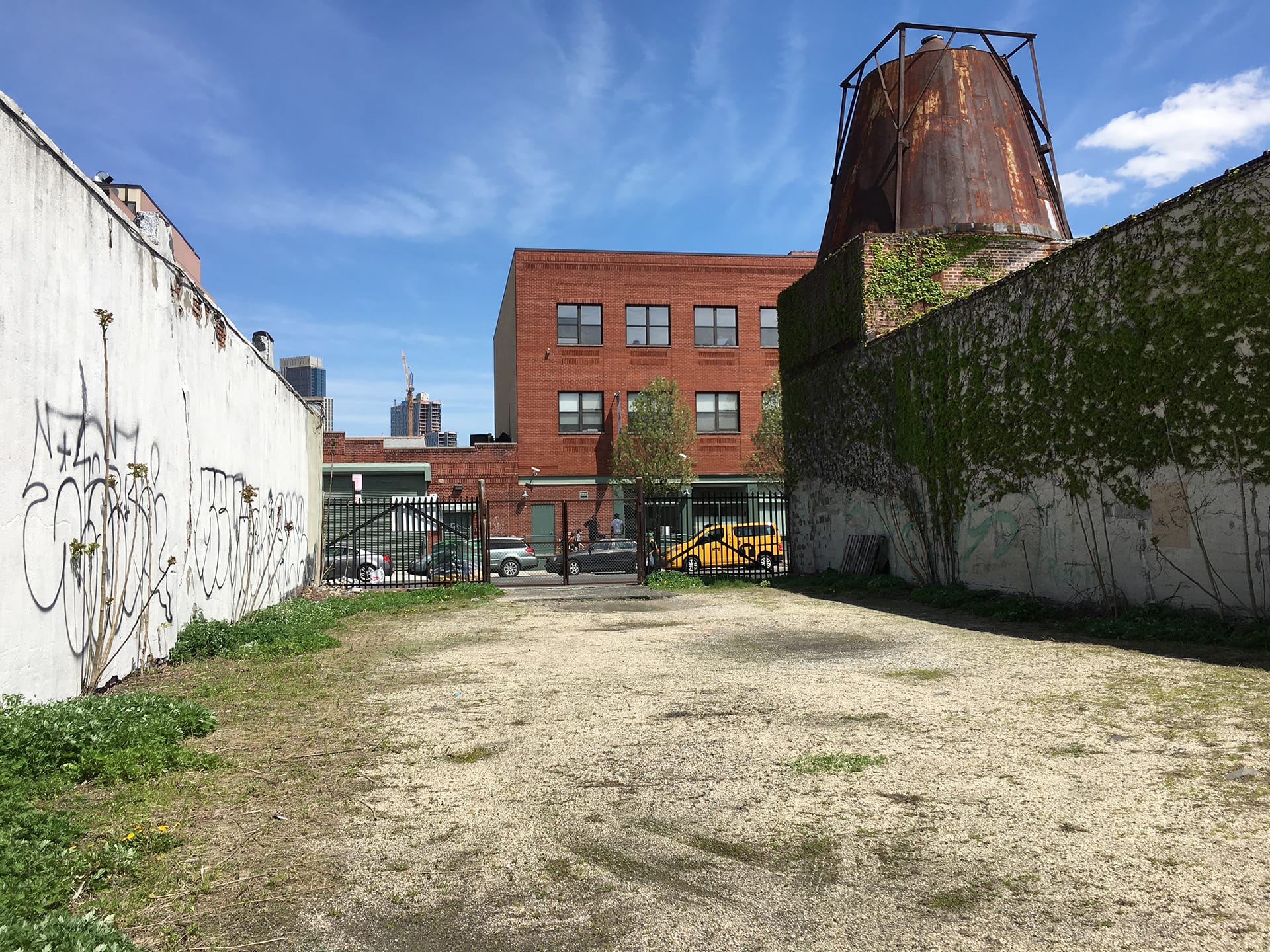 Empty gravel courtyard between two buildings in Gowanus, Brooklyn, with a gate separating the empty lot from the street.
