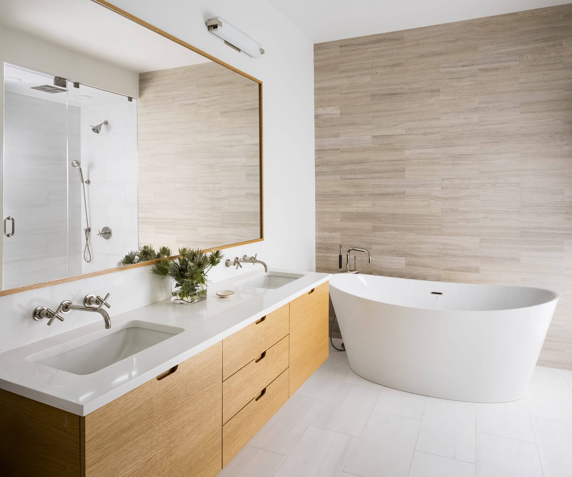Primary bathroom with a large wood vanity and matching mirror, freestanding white tub, and one tan tile accent wall