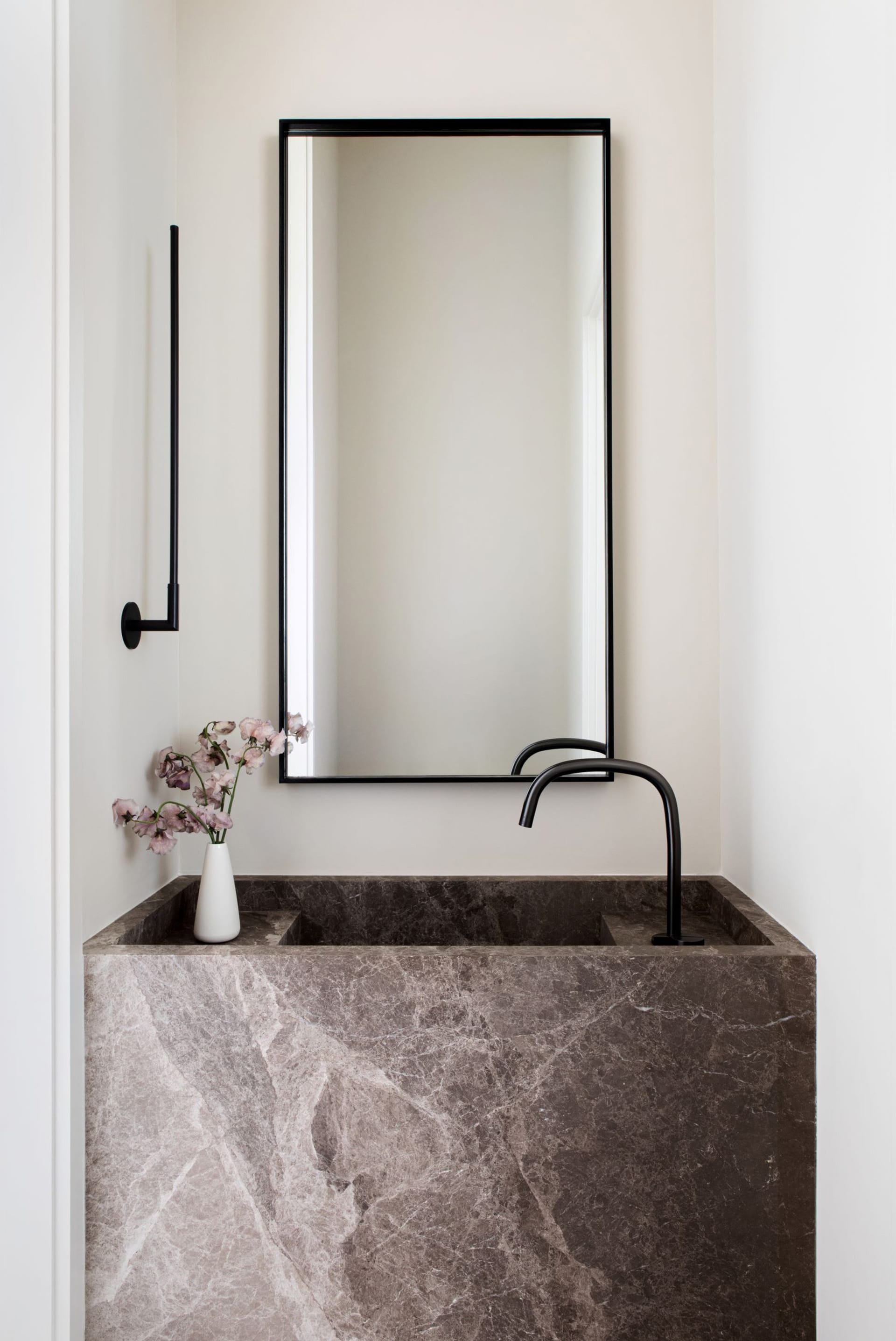Grey marble vanity with black faucet, towel rack, and mirror and a vase of flowers.