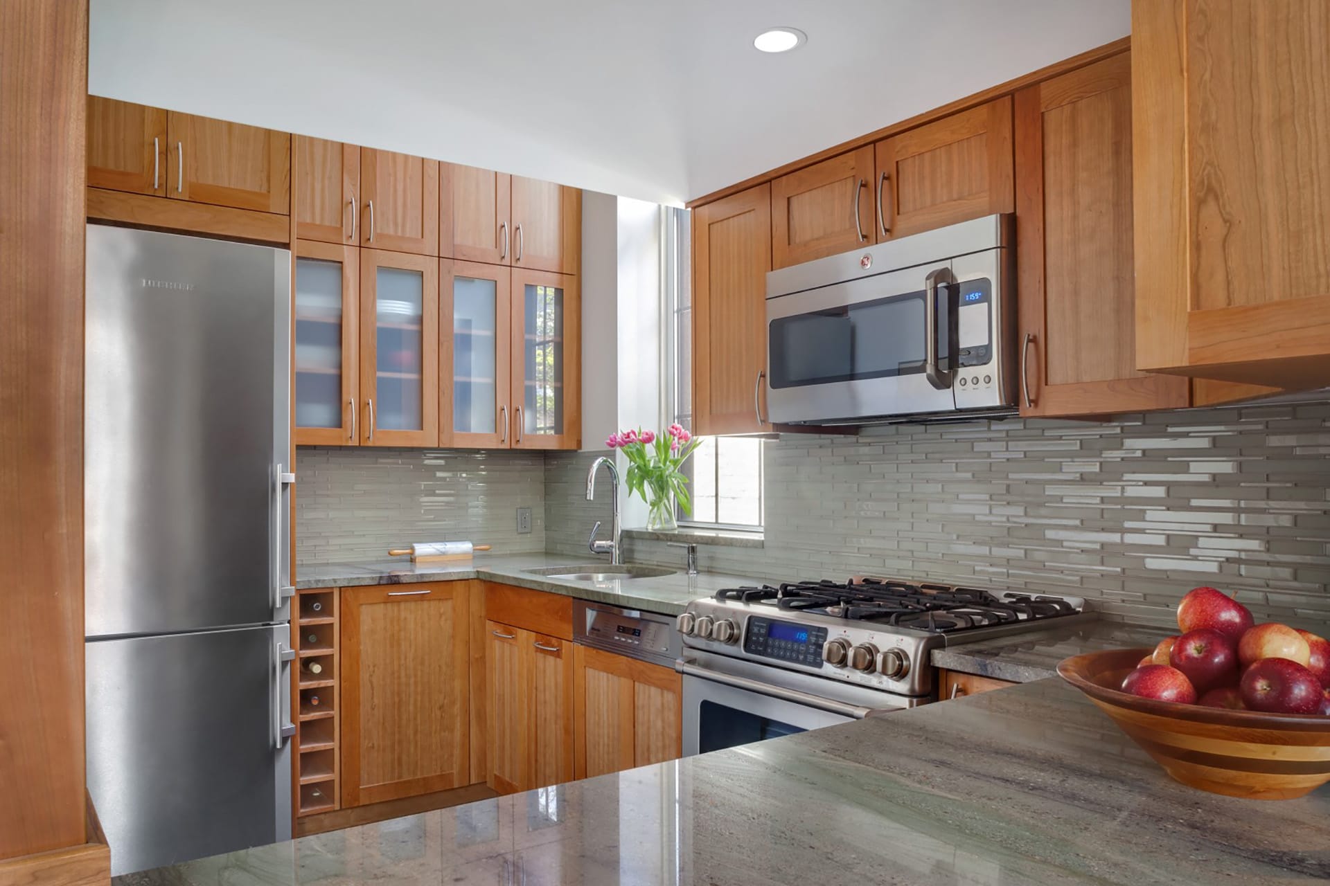 Kitchen after our renovation with natural wood cabinets, stainless steel appliances, and stone countertops.