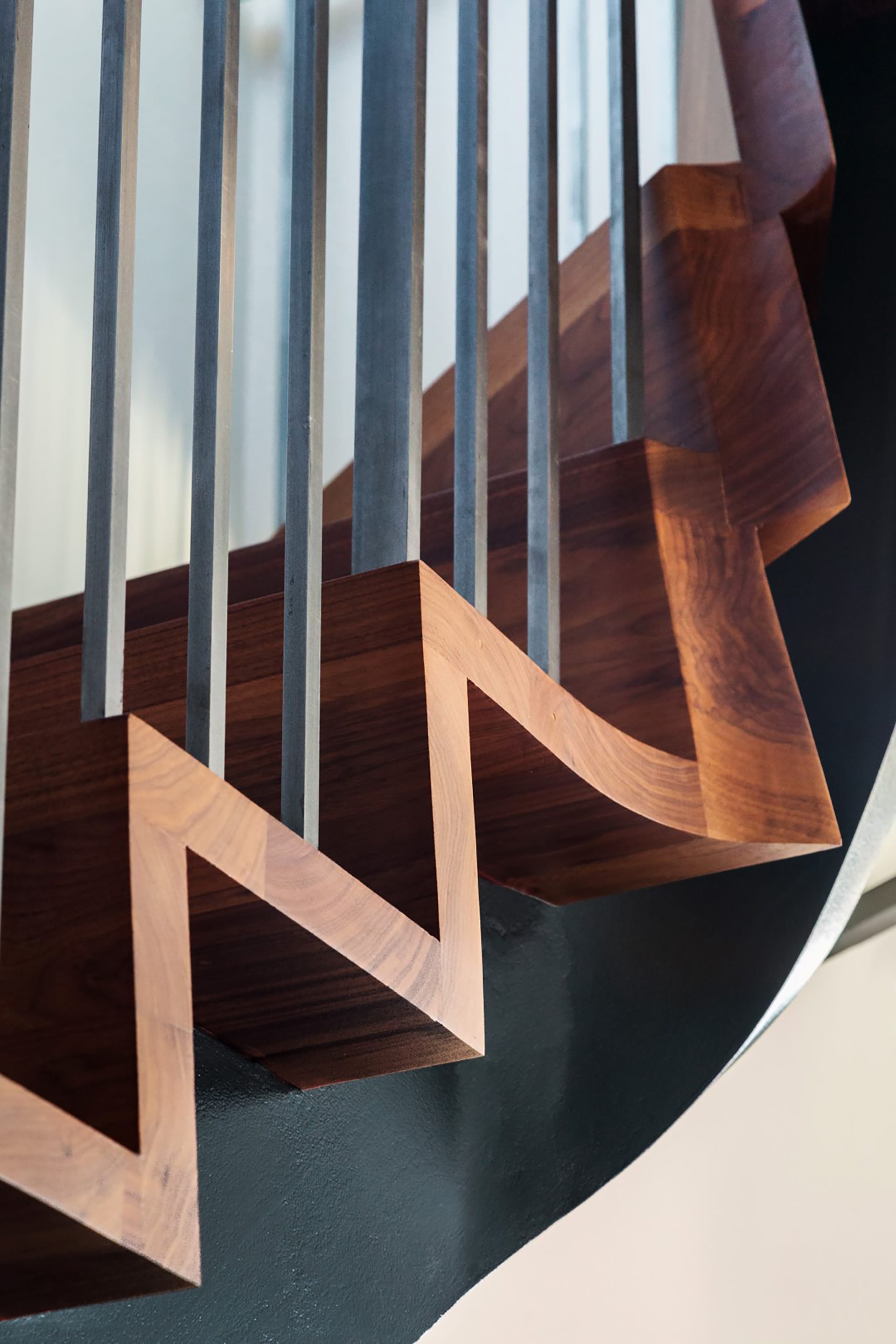 Sculptural staircase with black handrail and balusters and wood risers