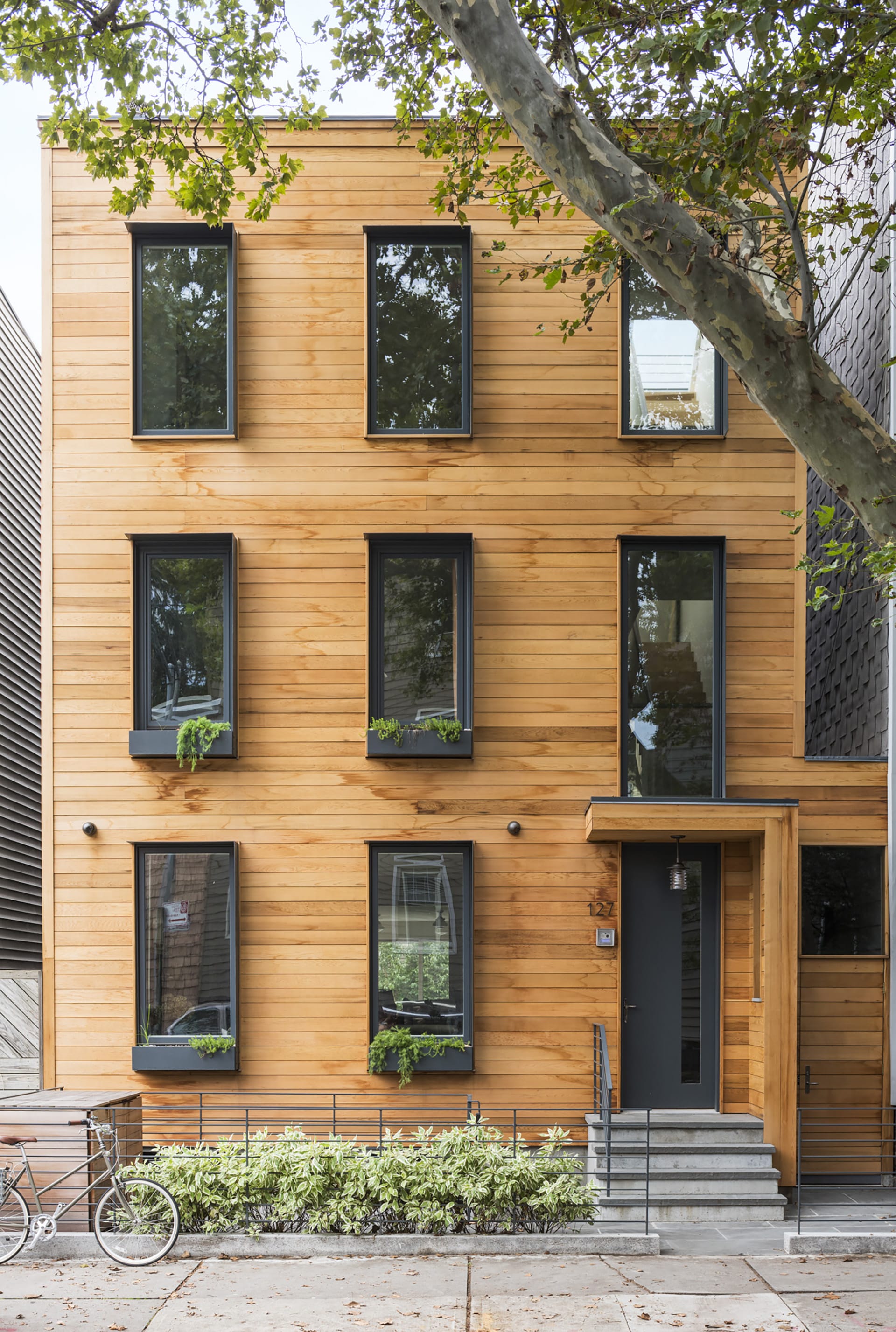 Exterior of a wood-framed Greenpoint townhouse with cedar siding, planters in front of the home and windows, and black window and door openings.