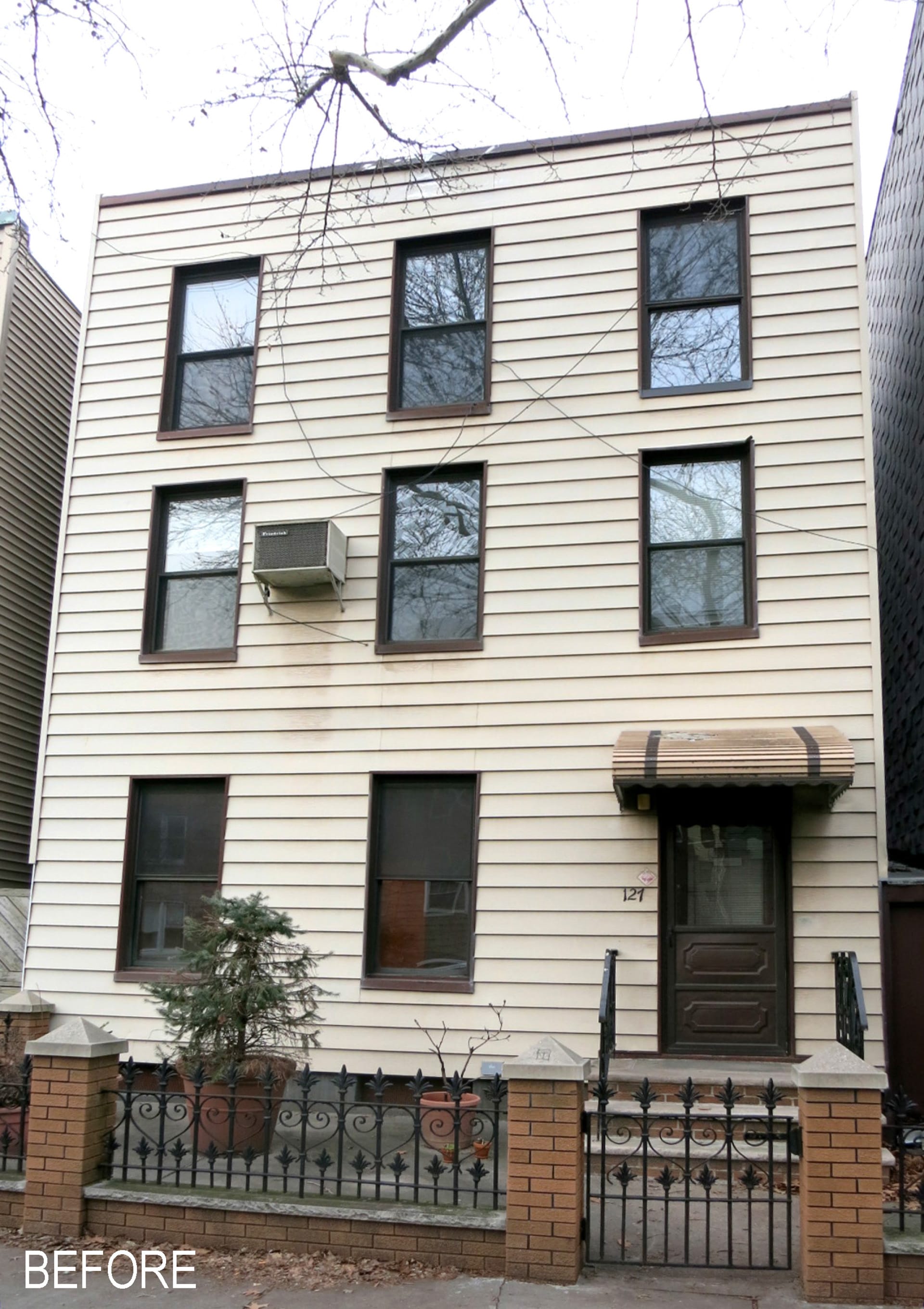 Greenpoint townhouse before our renovation, with white siding and dark window and door openings